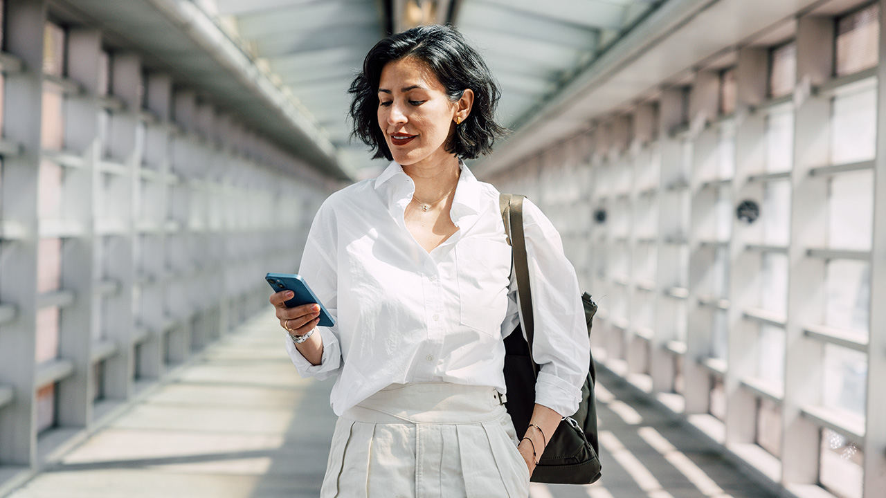 középkorú nő sétál telefonjával a kezében